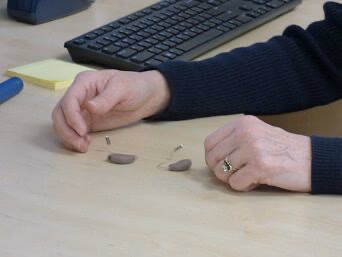 Julie displaying a pair of hearing aids at her desk